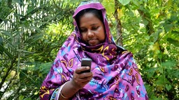 A woman looks down at a mobile phone in her hand.