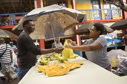 Woman stallholder selling bananas hands a bag to a man.