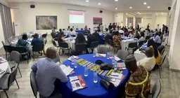 People sitting at tables facing a panel and a whiteboard behind them.