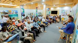 Four people holding microphones sit in front of a seated audience.