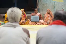 Woman sitting leg crossed on the floor hold a laptop in front of an audience of men