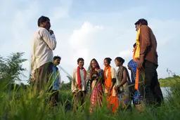 Smiling women and men standing in a field looking at a mobile phone