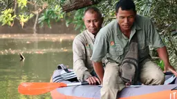 Two men in a dinghy out on water; one holding an oar.