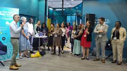 A groupo of people stand around a man speaking to the group.
