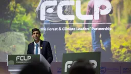 A suited man stands at a podium making a speech.