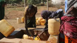 Man and woman fill up jerry cans with water from a fountain