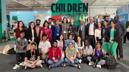 A group of people, largely young people, gather to pose for a photo, inside a conference venue.