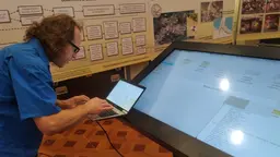 Man types in a laptop, in front of a big screen