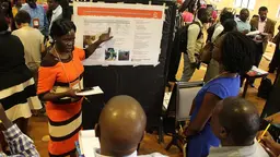 Woman talks and points at a poster behind her while people stand in front of her