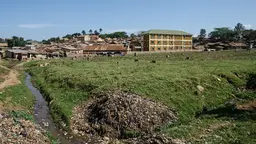Dirt and dirty canal next to a field. Informal buildings in the background