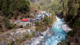 A small town sits beside a river with mountains in the background