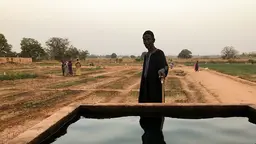Man, holding a wlaking stick, stands in front of a well full of water