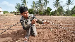 A man kneeling on the ground holding a hose