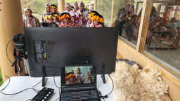 A group of people look at a TV screen, in front of which a computer shows how they appear on the screen.