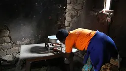 Woman bends over to light fir under a cooking pot.