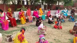 A group of women who are socially distanced and wearing protective masks, sit on benches and the grass.