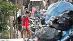 Woman walking a flooded road with piles of trash bags next to her.