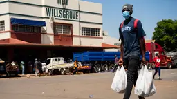 Man wearing a face mask walks carrying two shopping bags.