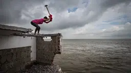 Man standing on a house roof holds a hammer.