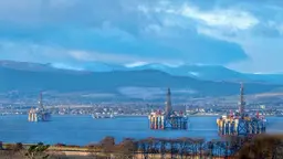 Oil rigs in water with mountains in background.