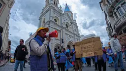 Man at a protest holds a megaphone leading a crowd, holding signs.