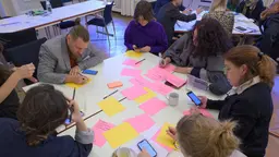 People sitting around a table writing on coloured pieces of paper.