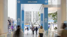 A timelapse photo that shows blurred people entering/leaving a building above which is a big sign saying 'Welcome'