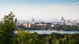 A view of Beijing across the river. There are trees and greenery in the foreground.