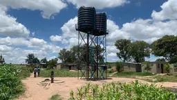 A tall metal water tower with several small brick buildings around it. 