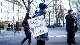 Climate protestor holding sign that reads "Act now or swim later"