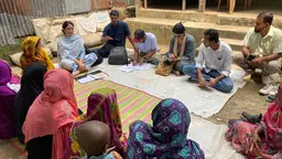 Group of people sitting down on the floor in a circle discussing during a workshop in Bangladesh.
