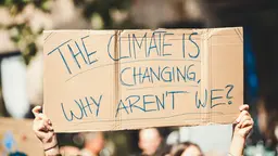 Person hold up sign saying 'The climate is changing, why aren't we?'.