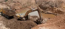 A digger in a mining quarry digs earth and transfers it to a lorry just behind it.