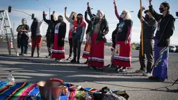 A group of Indigenous Women wearing traditional dress protesting outside, holding signs and raising their fists in the air