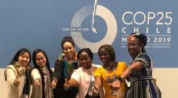 Smiling women gather in front of a climate change conference sign and give a thumbs up