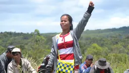 Member of local Indigenous community at protest, standing with a fist in the air.