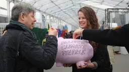 A woman holds a pink piggy bank in front of her, with the words 'Deliver climate finance' written on the front.