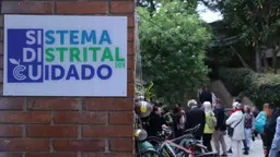 Image of sing on building, with people seen on the background. Sign reads 'Sistema Distrital de Cuidado'.