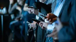 Journalists during a press conference, reading on their phones.