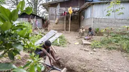 A worker installs a water pipe observed by two women.