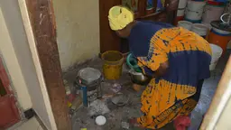 A woman bends over as she cooks in small poorly ventilated room.