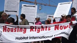 Protestors holding a big sign that reads 'Housing rights now! Habitat International Coalition'