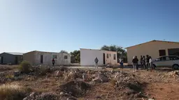 Houses being built in Namibia. Group of people standing looking at them, pointing and talking.