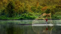 Community member in Indonesia casting a net over water from a boat, to catch fish.