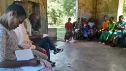 Community members during a meeting, sitting down, writing notes and discussing.