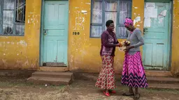 Two women standing in front of a seed bank, talking and laughing. They are wearing vibrant shades of pink and red.