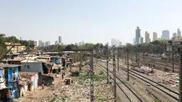Informal settlement in Mumbai situated next to train tracks with various electric wires going above it.