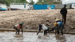 A group of workers work stand in a flooded road, with water up to their knees and vast swathes of mud in the background.