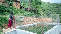 Woman standing at a gate of a new water collection reservoir built to help with climate resilience for vulnerable communities. 