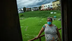 Woman sitting on a balcony wearing a face mask. Behind here, an informal neighbourhood of houses can be seen.